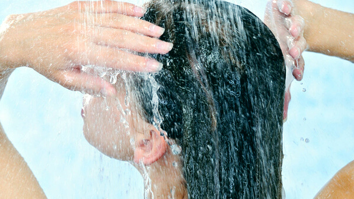Femme se lavant les cheveux sous une douchette
