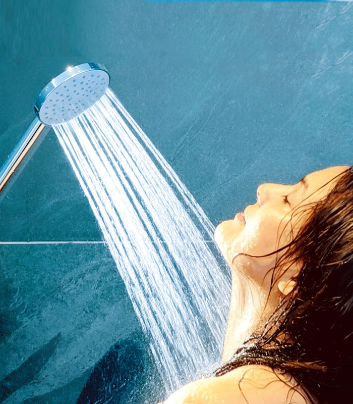 Wassersparender Duschkopf AquaClic Prosecco, strömt mit viel Wasser auf Gesicht, Hals und Körper einer jungen Frau vor türkisblauen Badezimmer-Kacheln.