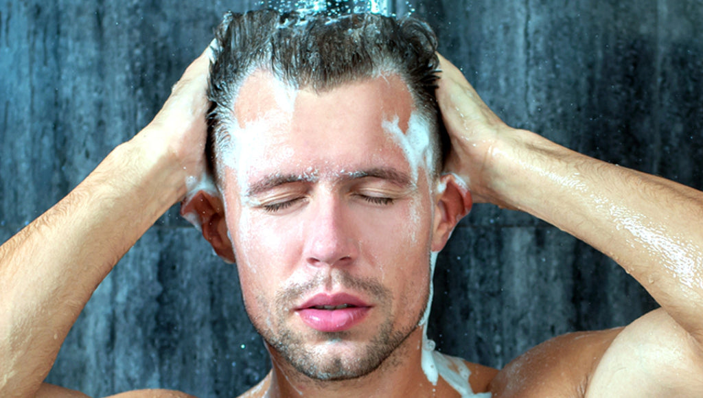 Junger Mann wäscht sich die Haare unter einer wassersparenden Duschbrause