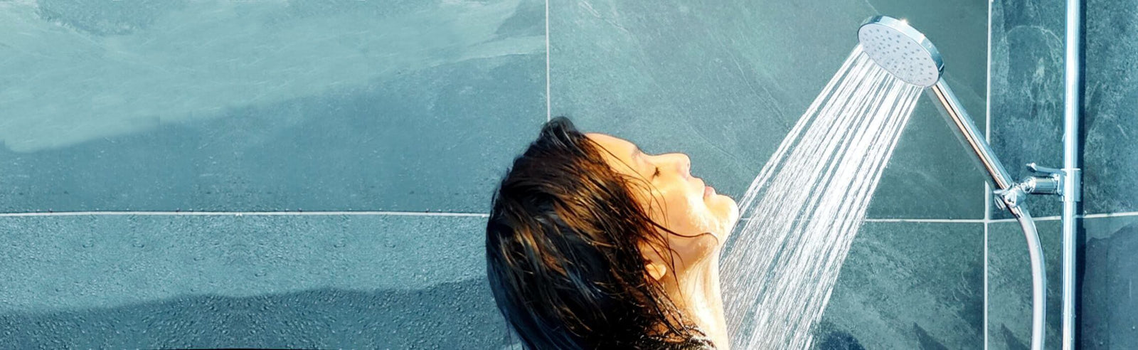 Junge Frau duchst genussvoll unter einer Duschbrause Prosecco mit vollem Strahl.