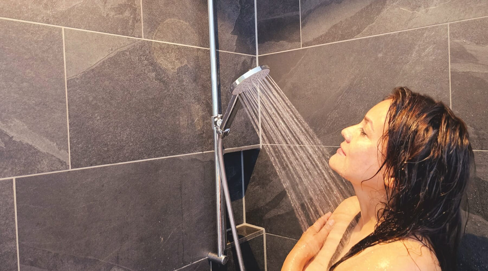 Junge Frau duscht genüsslich unter warmem Duschstrahl mit einer Sparbrause von AquaClic