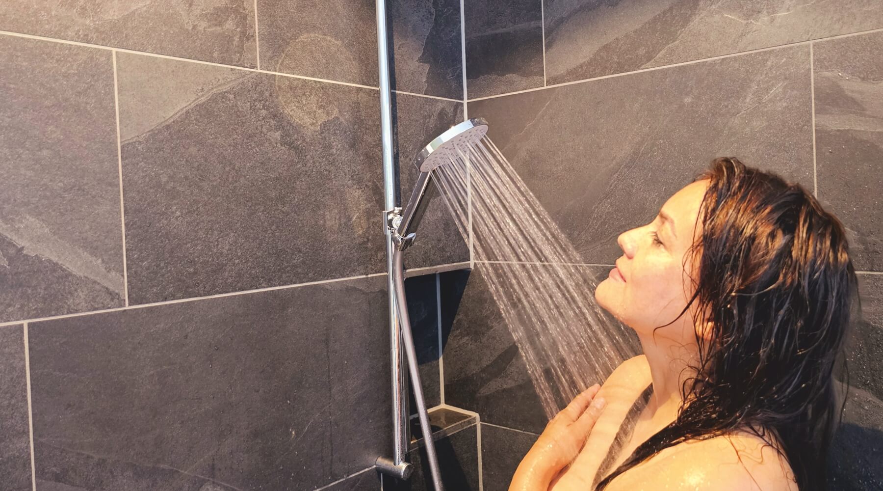 Junge Frau duscht genüsslich unter warmem Duschstrahl mit einer Sparbrause von AquaClic