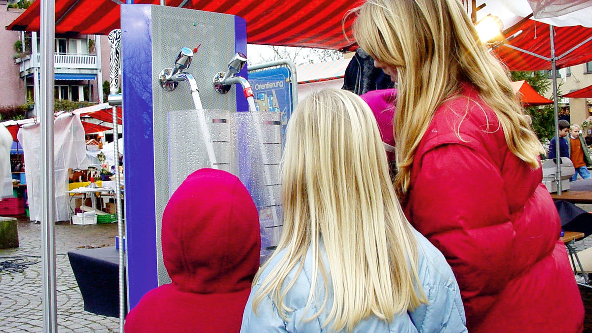 An einem Marktplatz zeigt eine Vorführerin die Funktion von AquaClic am Demonstrationsbrunnen